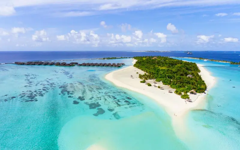 Vue aérienne d'une île tropicale avec une plage de sable blanc et une eau turquoise.