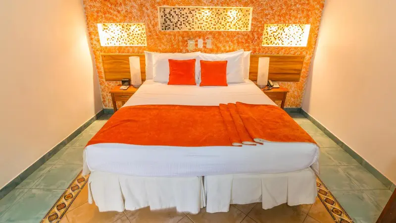Une chambre lumineuse avec un grand lit recouvert d'une courtepointe blanche et de coussins orange.