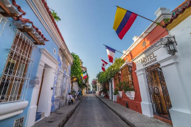 Rue colorée bordée de bâtiments coloniaux et de drapeaux flottant au vent.