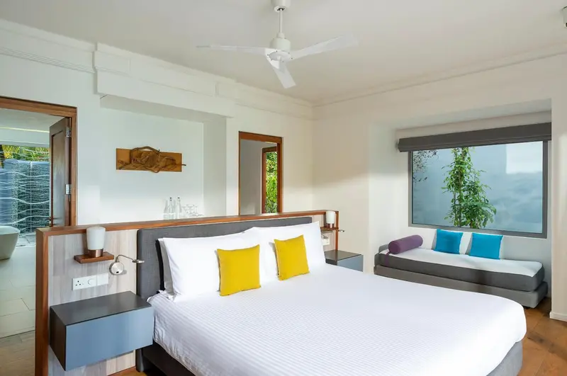 Chambre lumineuse avec un grand lit et un espace détente près de la fenêtre.