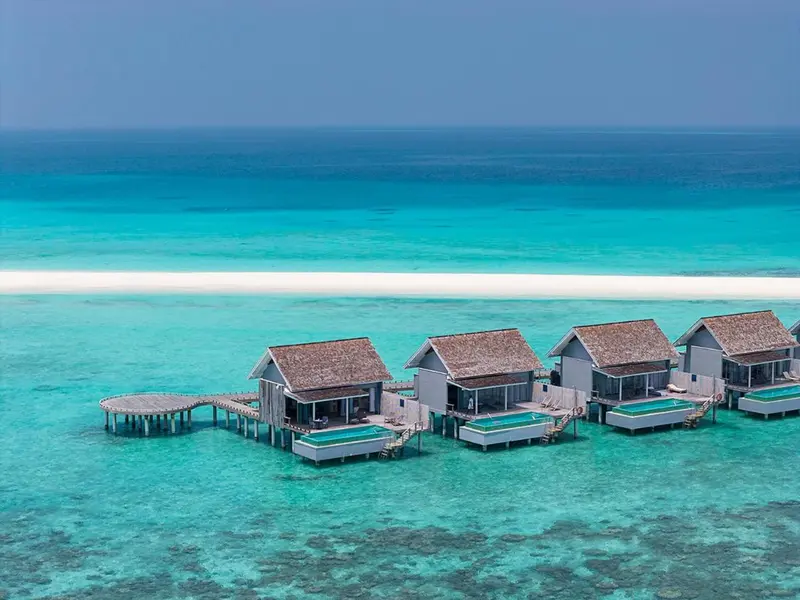 Maisons sur pilotis au-dessus d'une eau turquoise et d'un récif corallien.