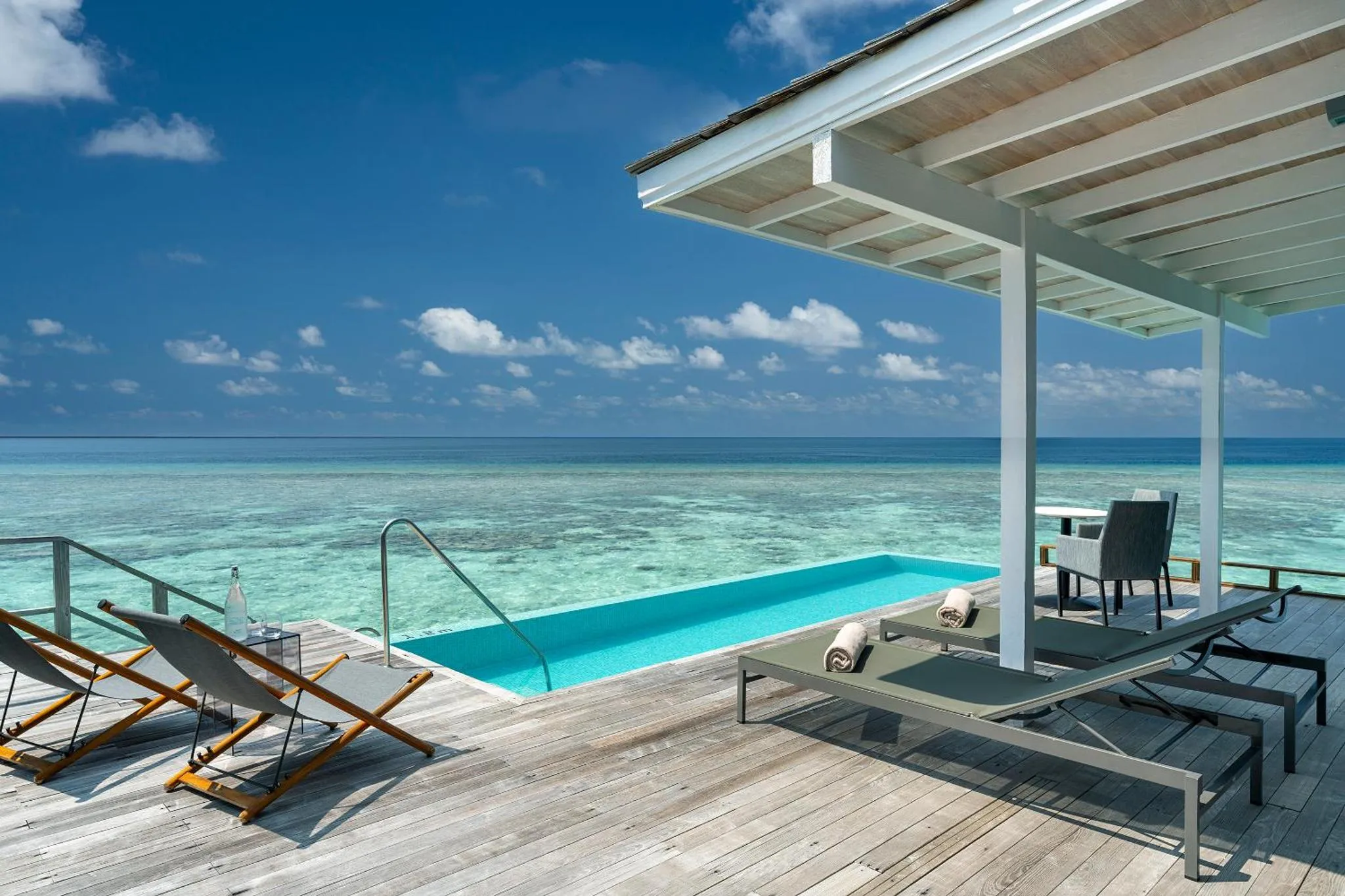 Terrasse en bois avec piscine et chaises longues face à la mer.