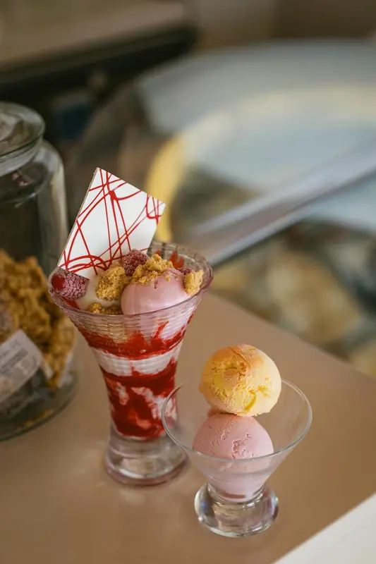 Deux coupes glacées décorées de fruits rouges et de biscuits sont présentées sur une table.