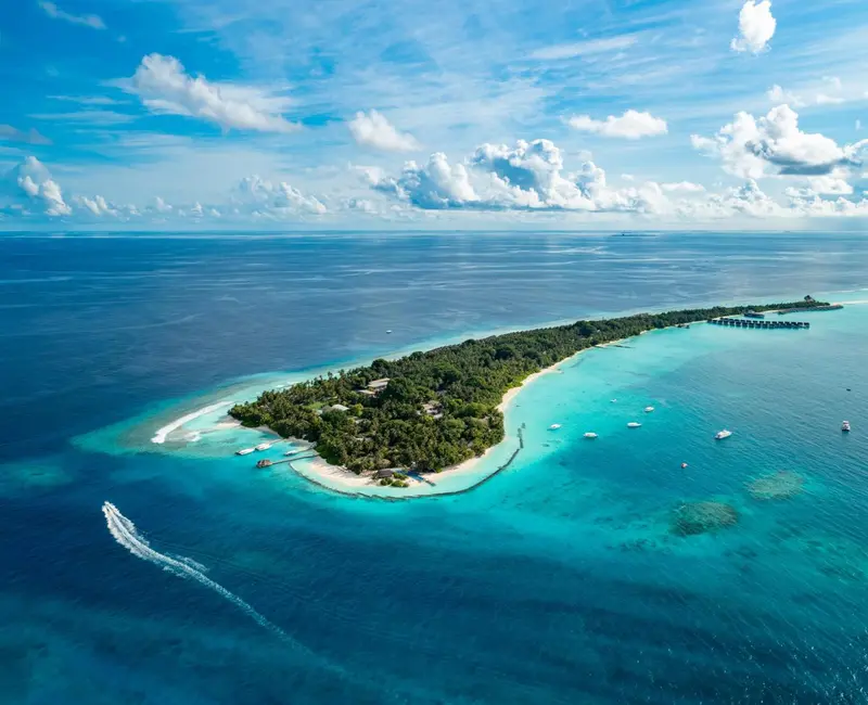 Vue aérienne d'une île tropicale entourée d'une eau turquoise et de quelques embarcations.