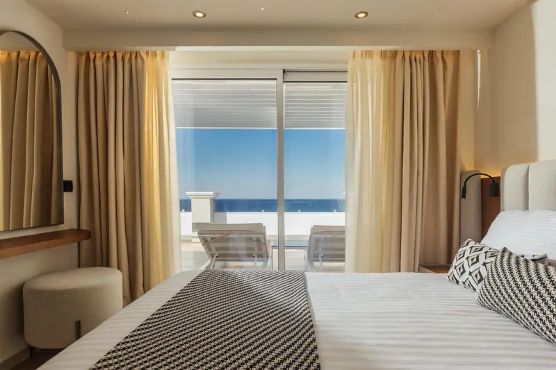 Chambre lumineuse avec un grand lit donnant sur une vue mer.