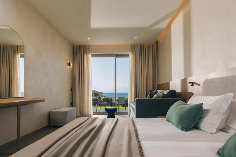 Une chambre lumineuse avec un grand lit et un canapé face à une baie vitrée.