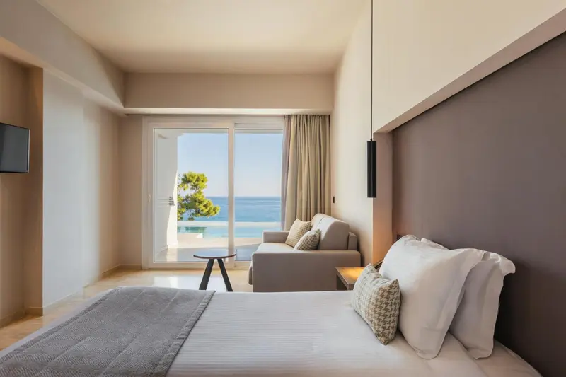 Une chambre lumineuse avec un lit fait et un coin salon donnant sur la mer.