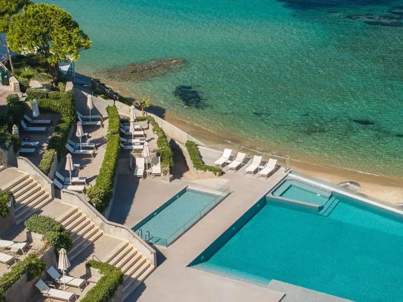 Terrasse avec chaises longues surplombant une plage et une piscine.