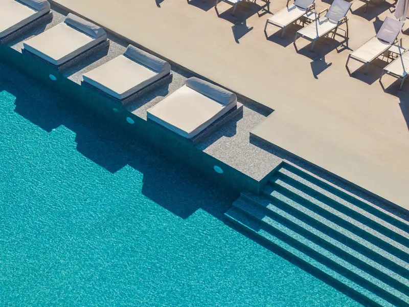 Transats blancs alignés au bord d'une piscine turquoise et de ses marches.