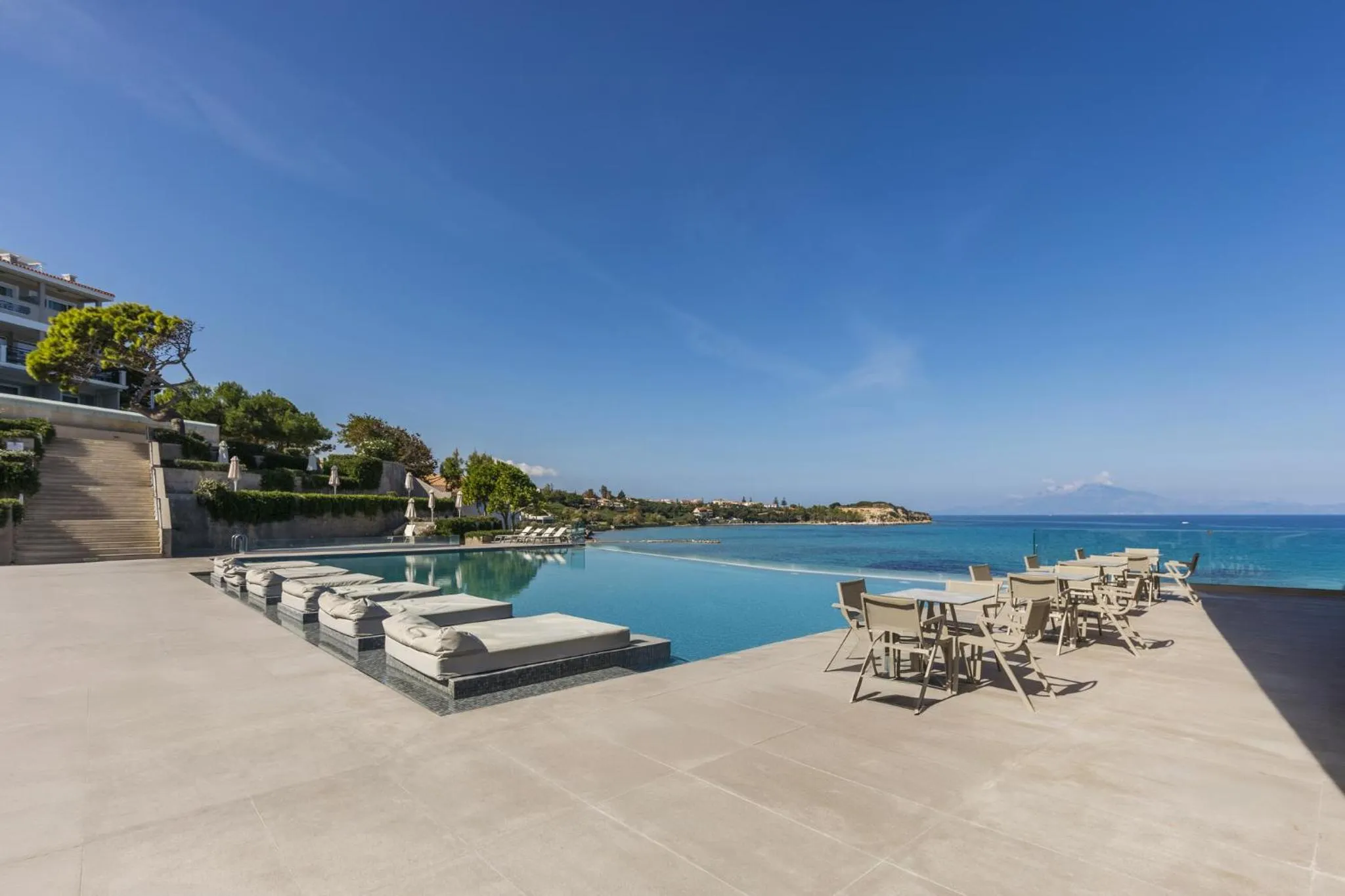 Terrasse avec transats et tables près d'une piscine à débordement donnant sur la mer.