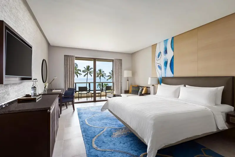 Chambre lumineuse avec un grand lit et vue sur la mer par une baie vitrée.