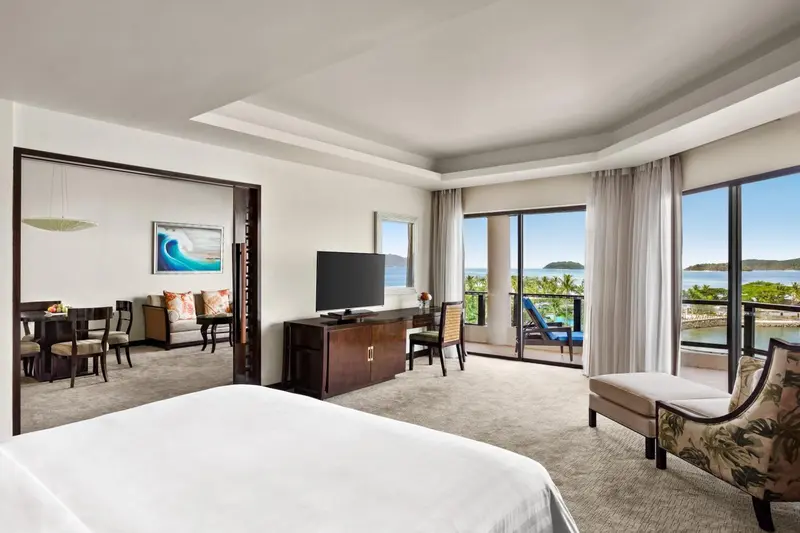 Une chambre lumineuse avec un grand lit et un espace salon attenant.