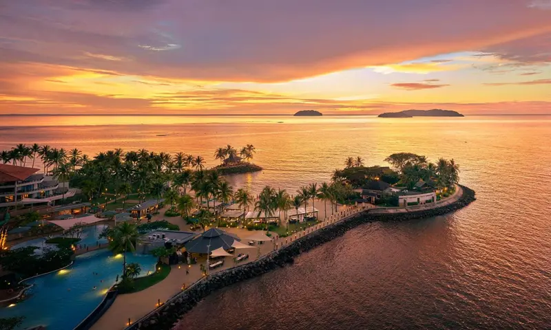 Vue aérienne d'un complexe hôtelier au coucher du soleil sur une côte tropicale.