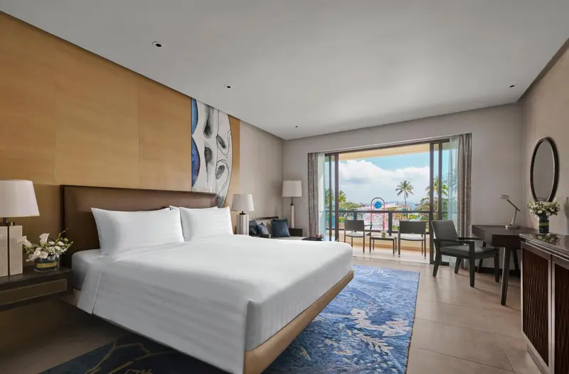 Chambre lumineuse avec un grand lit et une vue sur la végétation tropicale.