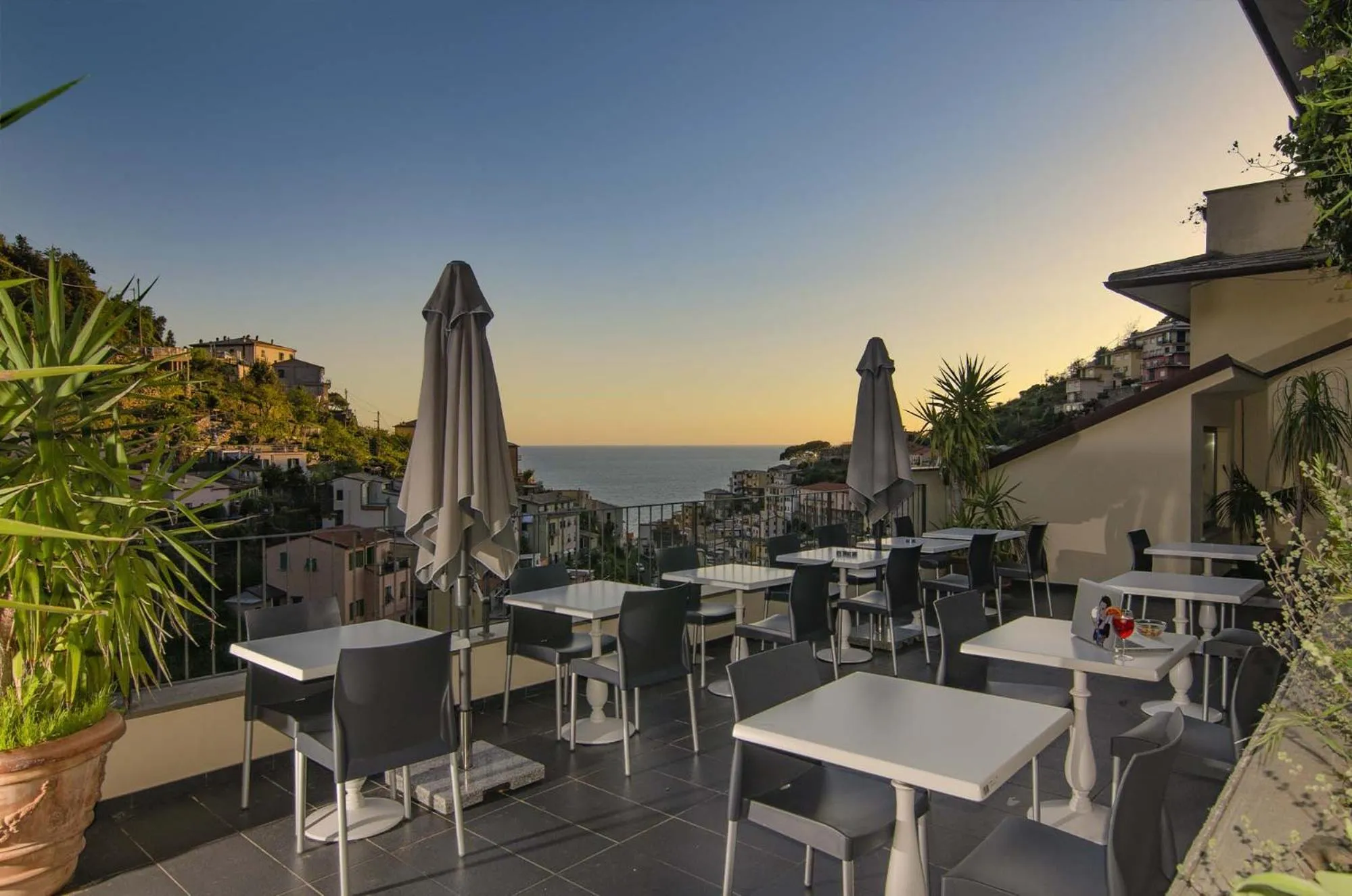Terrasse avec tables et chaises donnant sur la mer au coucher du soleil.