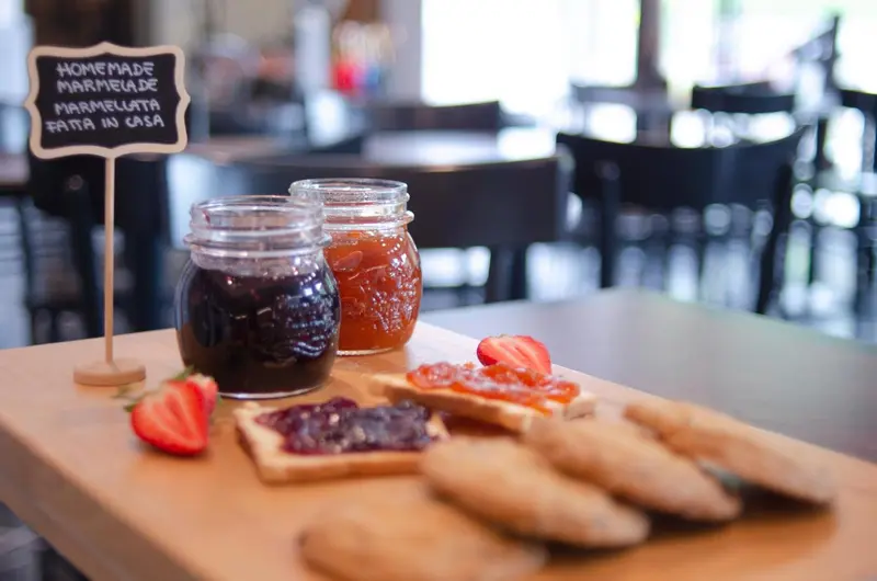 Des pots de confiture maison et des tartines sont présentés sur une table en bois.