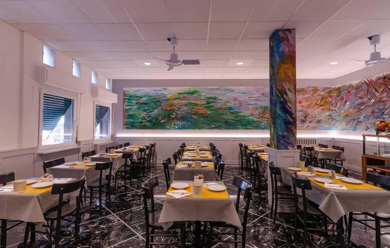 Une salle de restaurant lumineuse avec des tables dressées et une décoration murale abstraite.