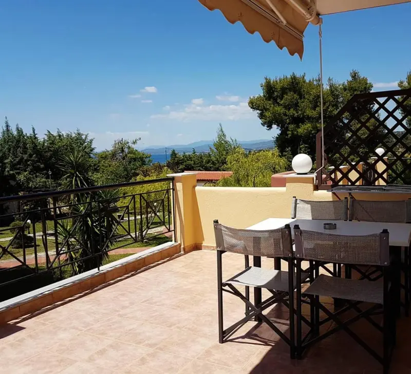 Terrasse avec table et chaises donnant sur un paysage verdoyant et la mer.