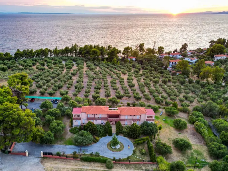 Vue aérienne d'un bâtiment bas entouré de végétation et surplombant la mer au coucher du soleil.