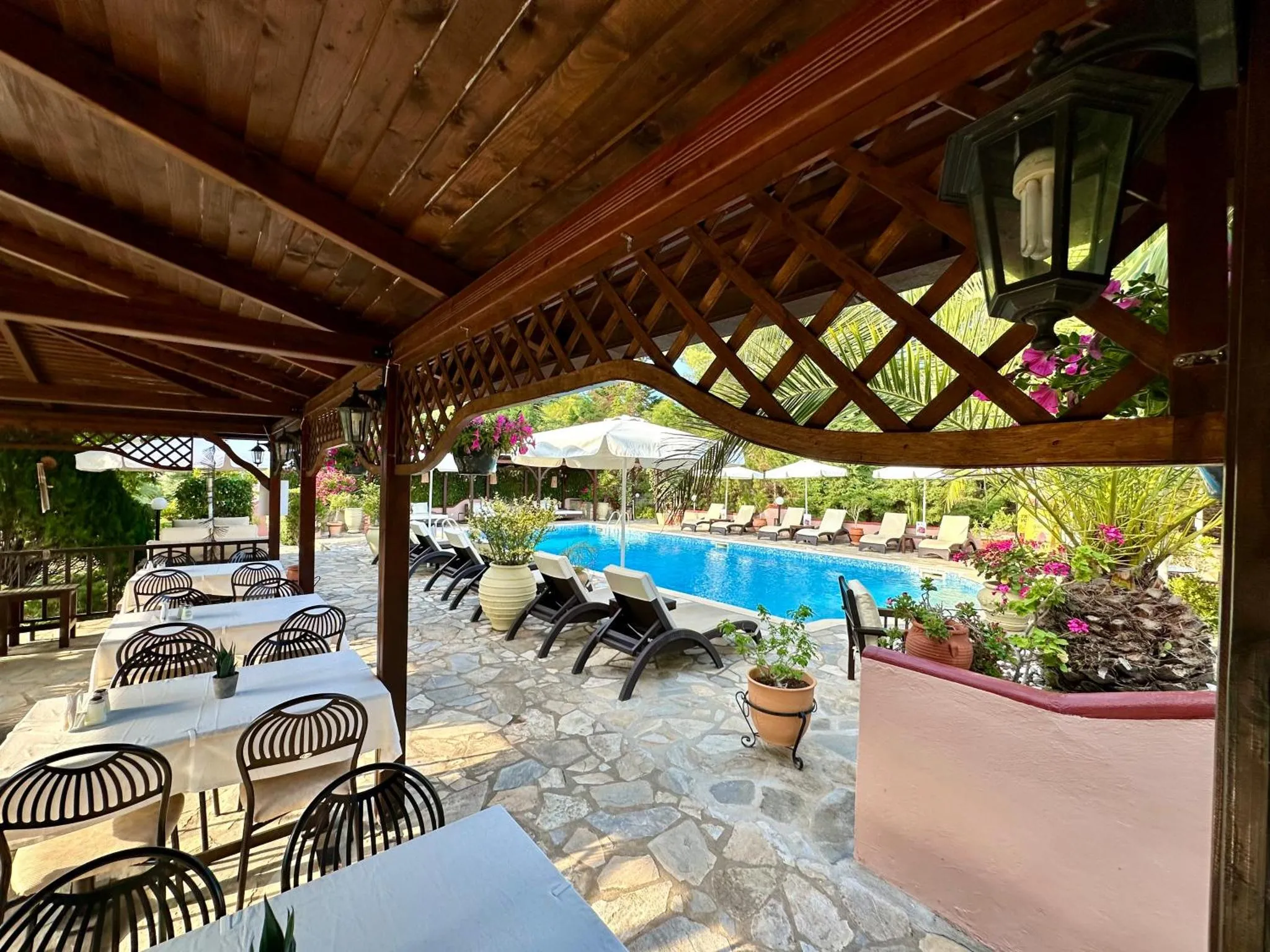 Une terrasse ombragée avec des tables et des chaises donnant sur une piscine.