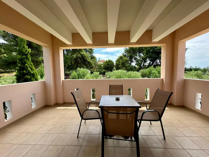 Une terrasse ombragée offre une vue sur la végétation et le ciel bleu.