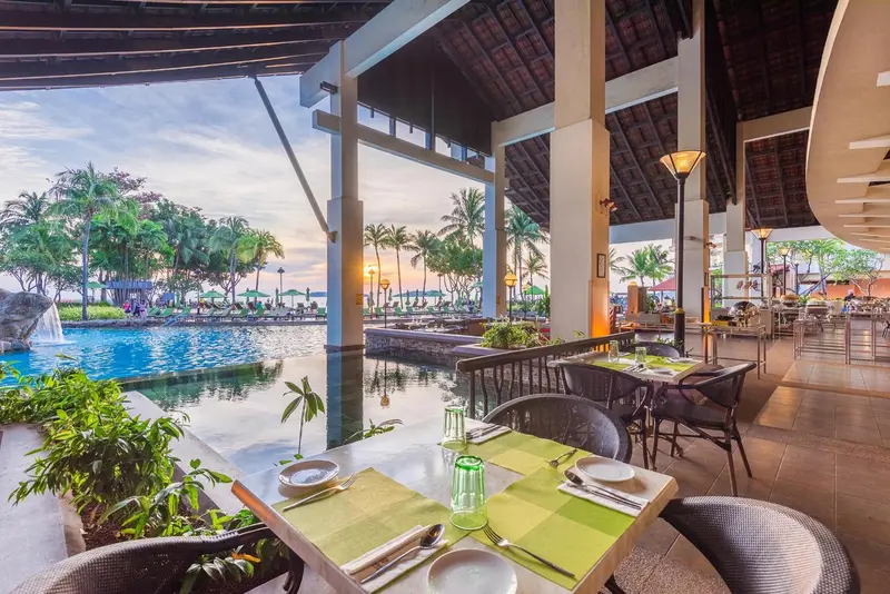 Tables dressées en terrasse avec vue sur une piscine et la mer au loin.