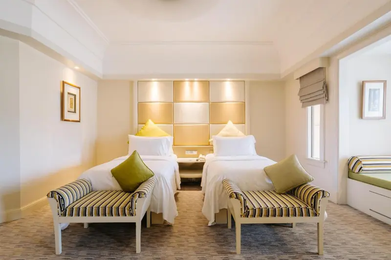 Chambre lumineuse avec deux lits simples et des fauteuils.