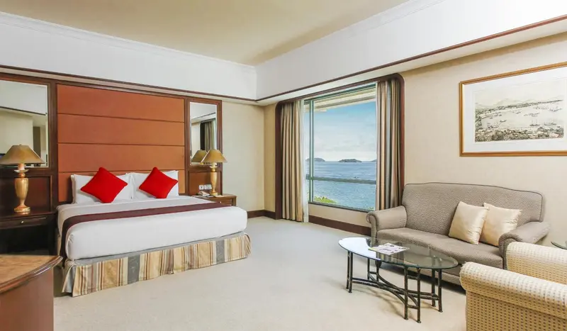 Chambre lumineuse avec un lit double et un coin salon donnant sur une vue mer.