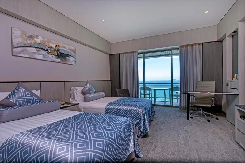 Chambre moderne avec deux lits et vue sur la mer par une grande baie vitrée.