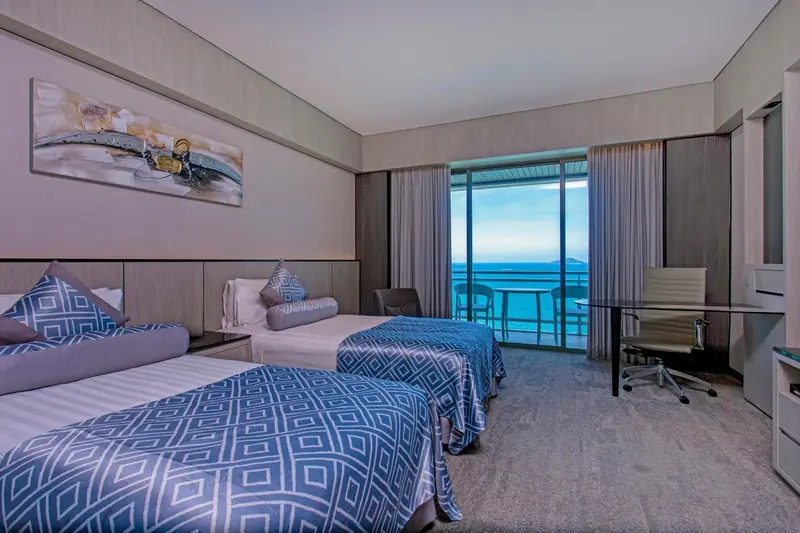 Chambre avec deux lits et vue sur la mer depuis un balcon.
