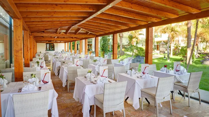 Une salle à manger extérieure avec des tables dressées et des chaises en osier.