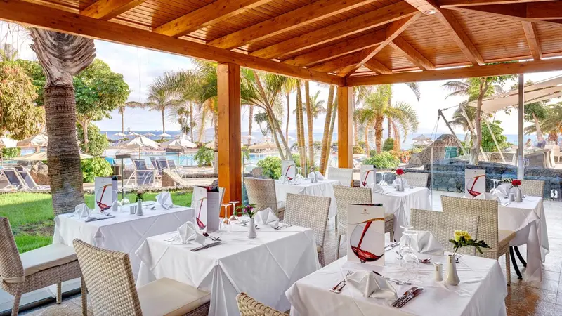 Une salle à manger extérieure avec des tables dressées face à un paysage tropical.