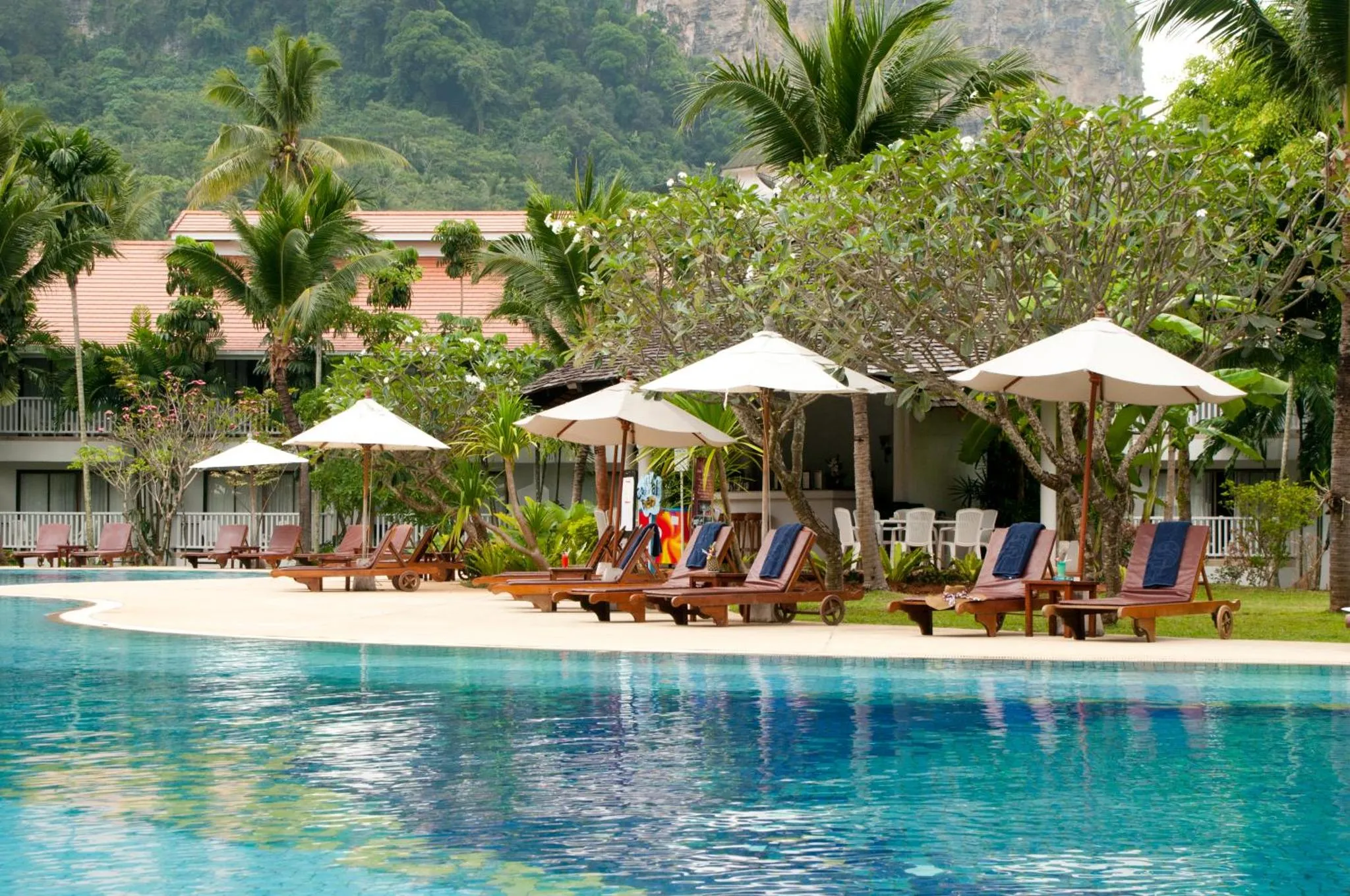 Transats et parasols bordent une piscine turquoise dans un cadre tropical.