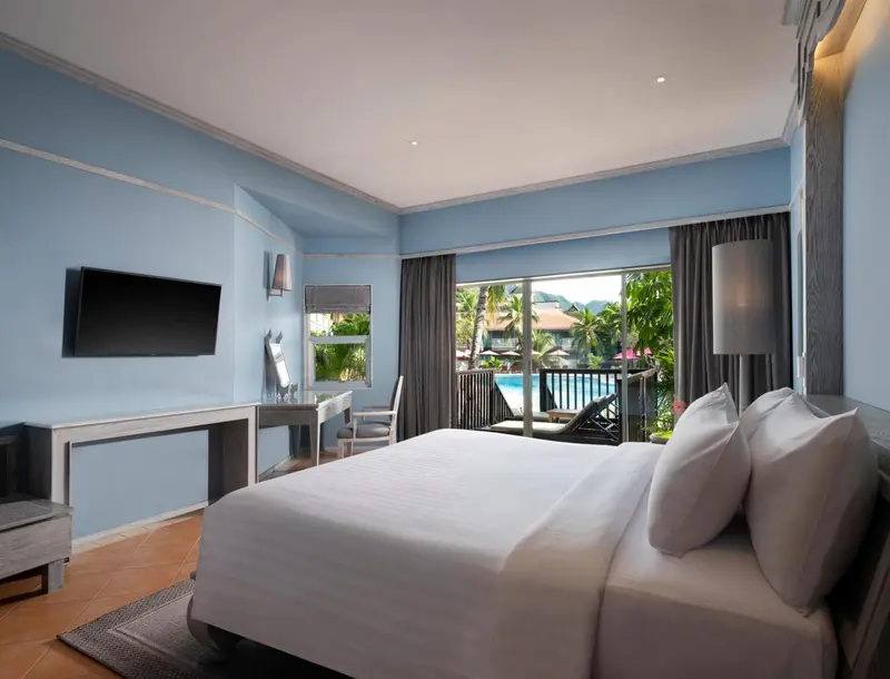 Une chambre lumineuse avec un lit king-size donnant sur une vue verdoyante et une piscine.
