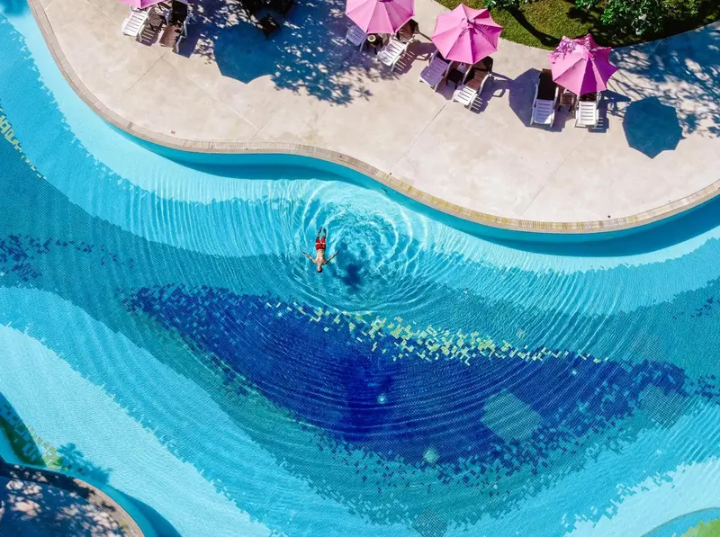 Vue aérienne d'une piscine sinueuse avec une personne allongée à la surface de l'eau.