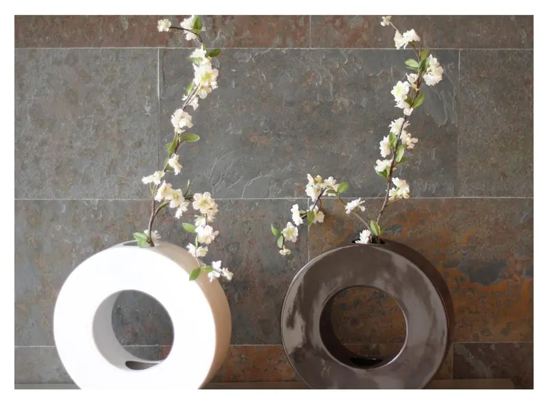 Deux vases contemporains avec des branches fleuries sur un mur texturé.