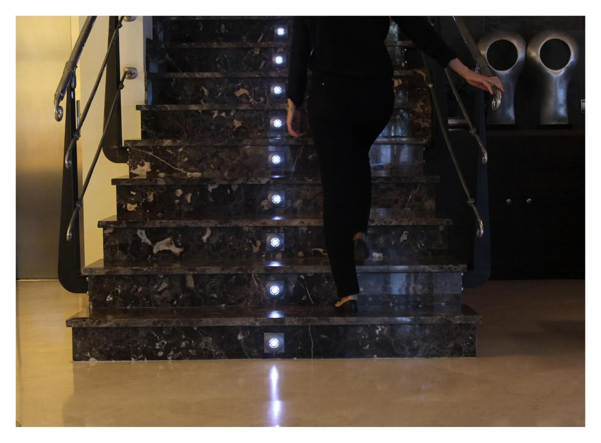 Une personne monte un escalier en marbre éclairé par des lumières intégrées.