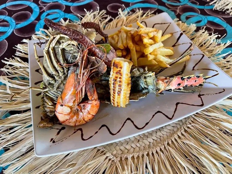 Assiette généreuse de fruits de mer grillés et de frites, décorée de verdure et de sauce.