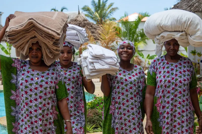 Quatre femmes souriantes portent des piles de linge sur leur tête.