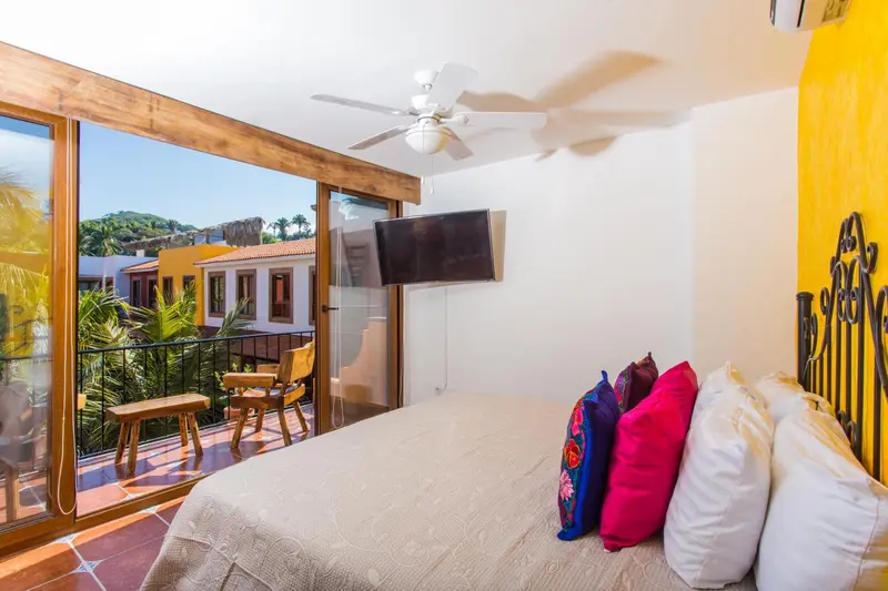 Une chambre lumineuse avec un lit décoré de coussins colorés et un accès à un balcon.