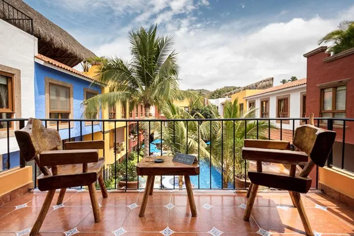 Terrasse avec mobilier en bois donnant sur une piscine et des bâtiments colorés.