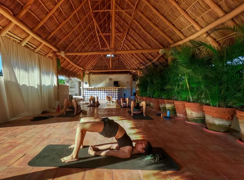 Une salle spacieuse abritée sous un toit de chaume accueille une séance de yoga.