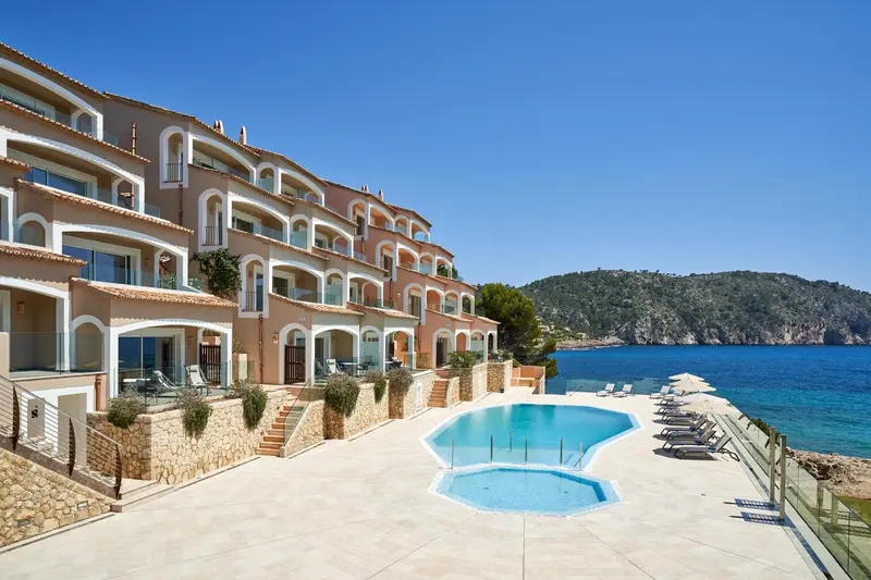Bâtiment beige avec balcons donnant sur une piscine et la mer.