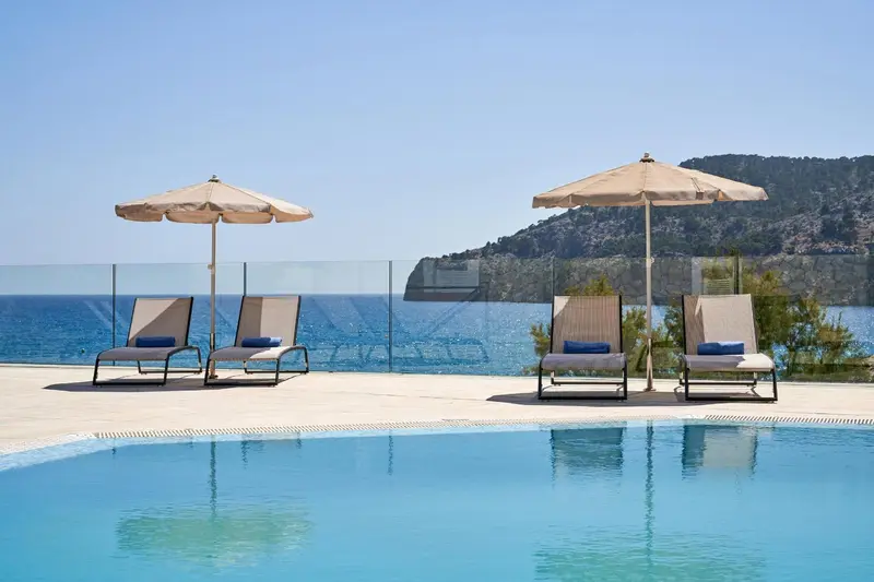 Transats et parasols disposés au bord d'une piscine avec vue sur la mer.