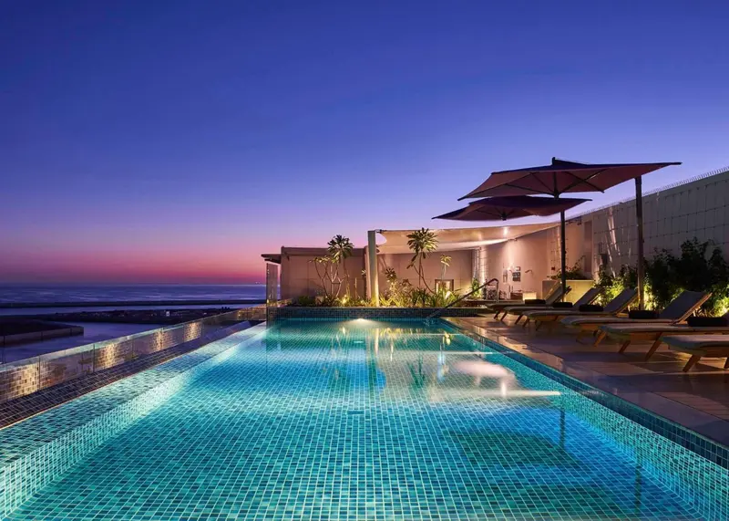 Piscine à débordement avec transats et parasols au crépuscule.
