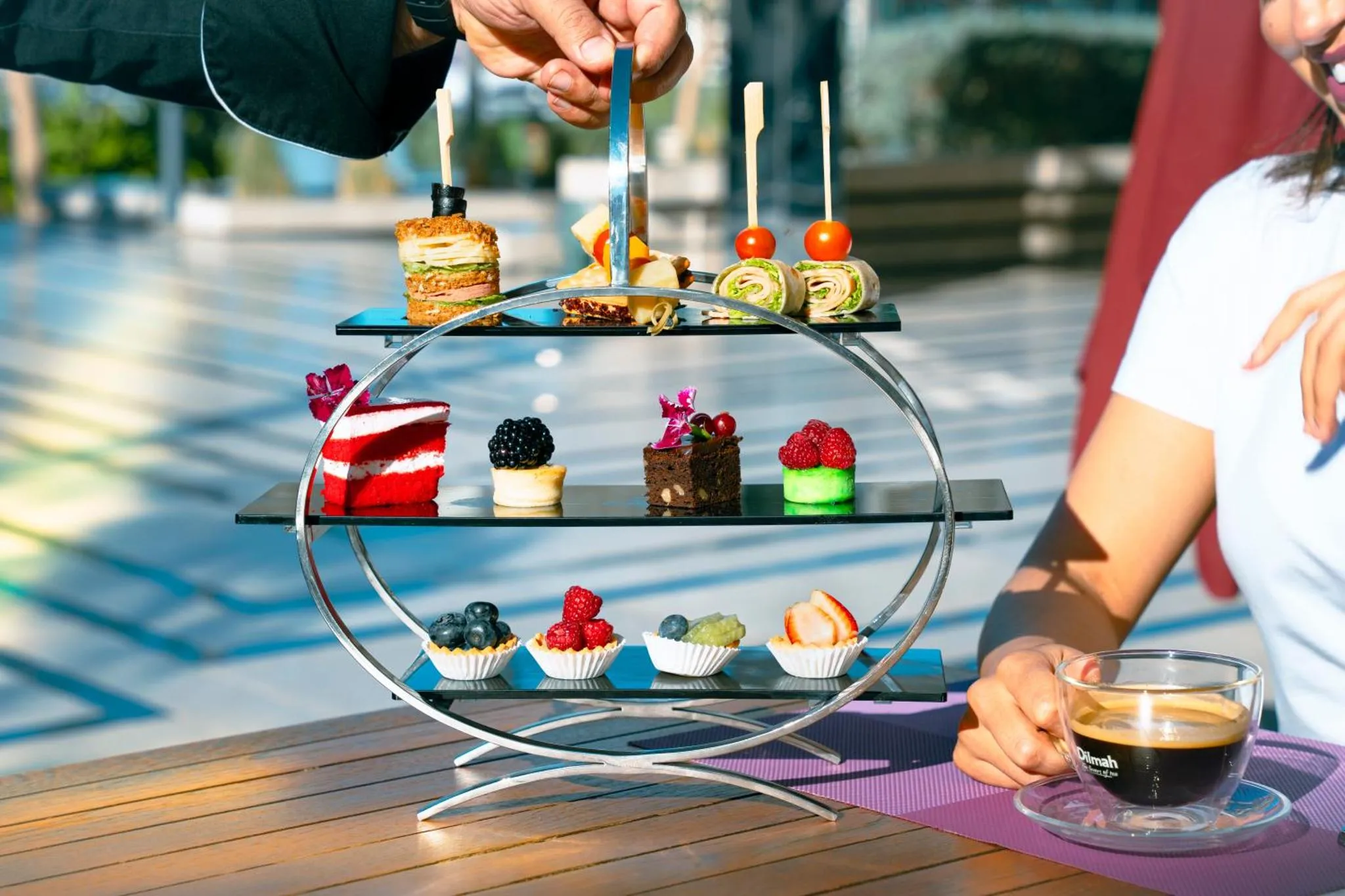 Présentation de petites bouchées et pâtisseries sur un présentoir à étages, avec une tasse de café.