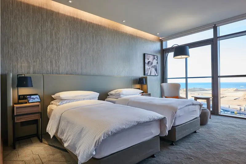 Chambre moderne avec deux lits simples et une grande fenêtre donnant sur la mer.