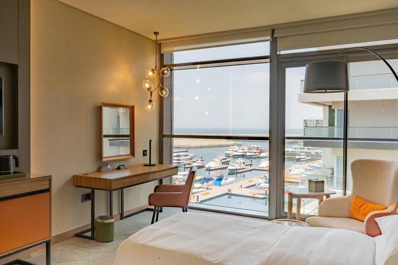 Une chambre lumineuse avec un coin lecture donnant sur un port de plaisance.