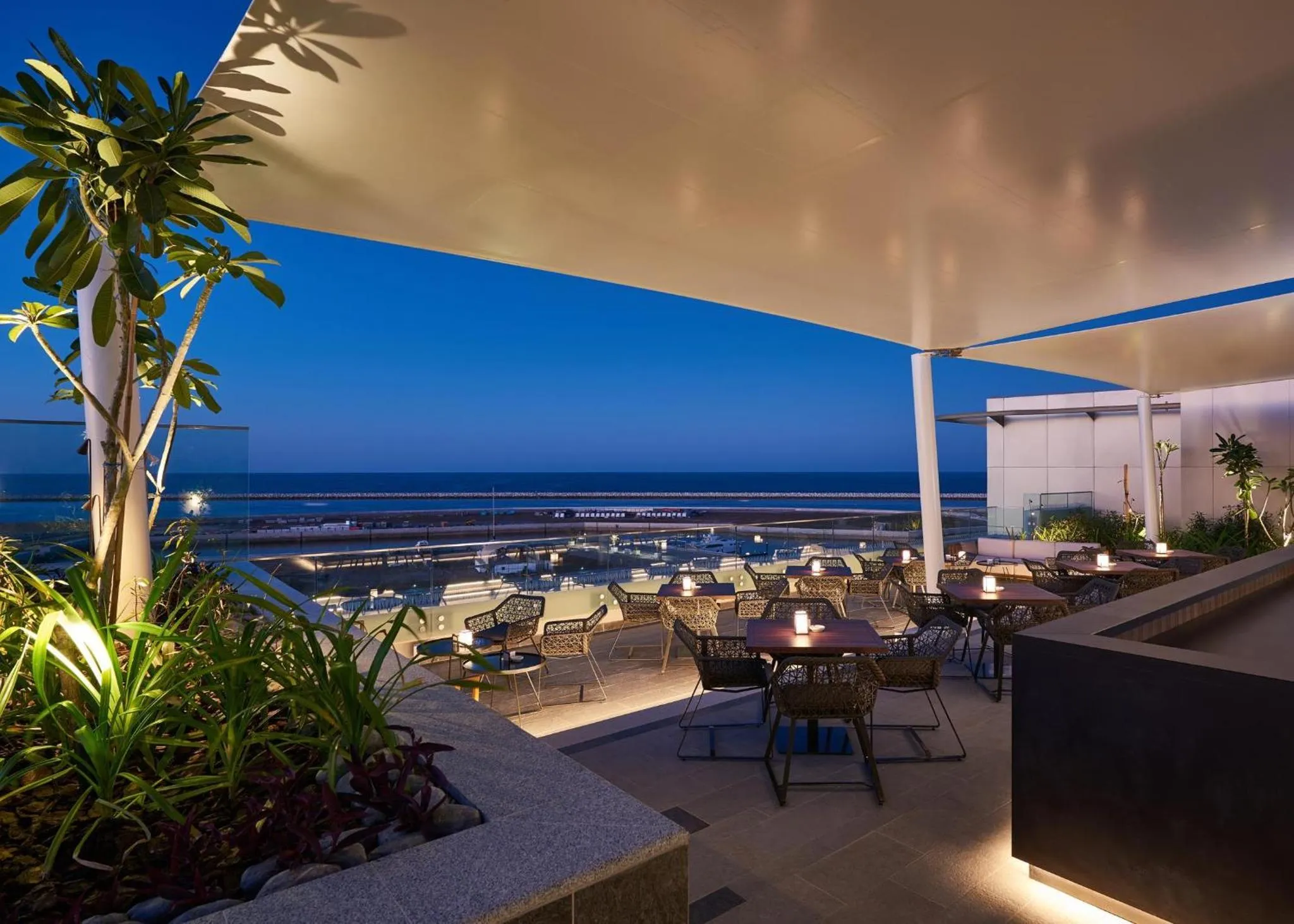 Terrasse aménagée avec tables et chaises face à la mer au crépuscule.