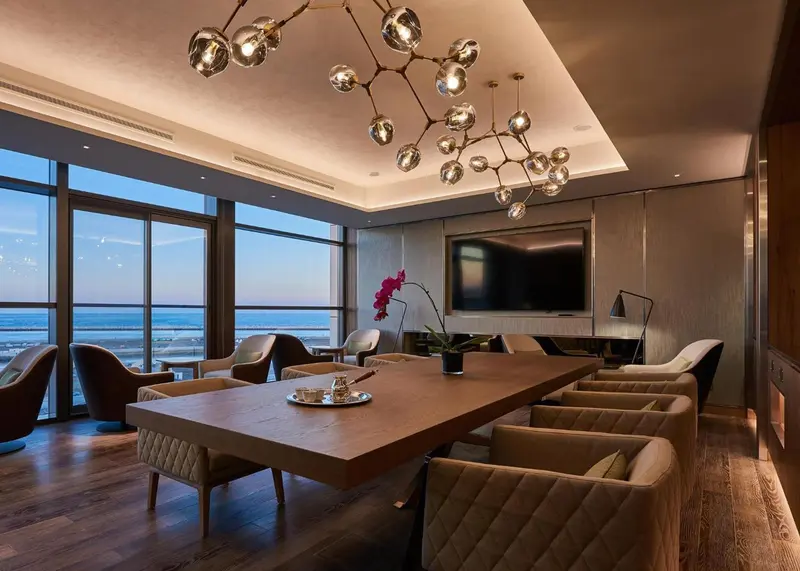 Une grande table à manger en bois se trouve dans un espace de vie lumineux avec une vue sur la mer.
